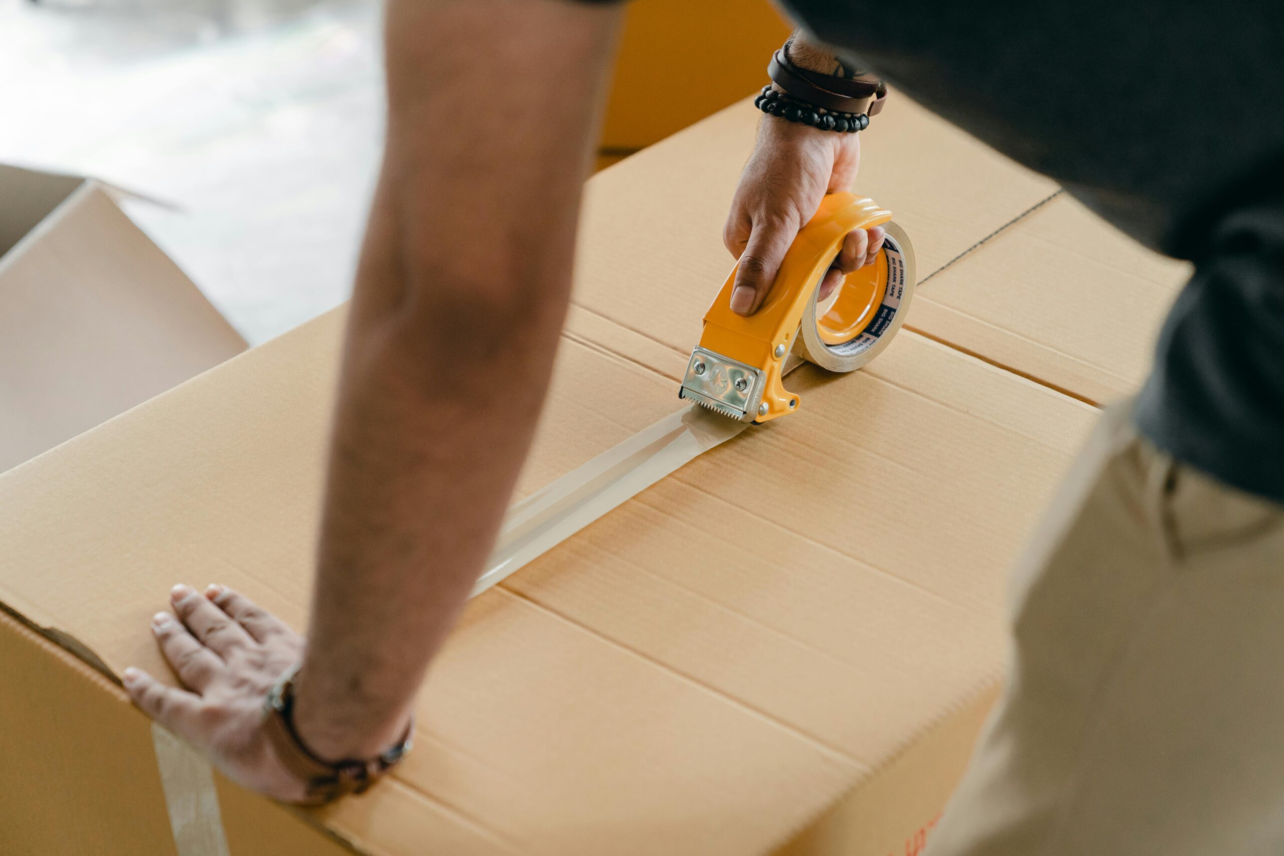 Man using packing tape to seal a cardboard box indoors. Ideal for moving or shipping concepts.